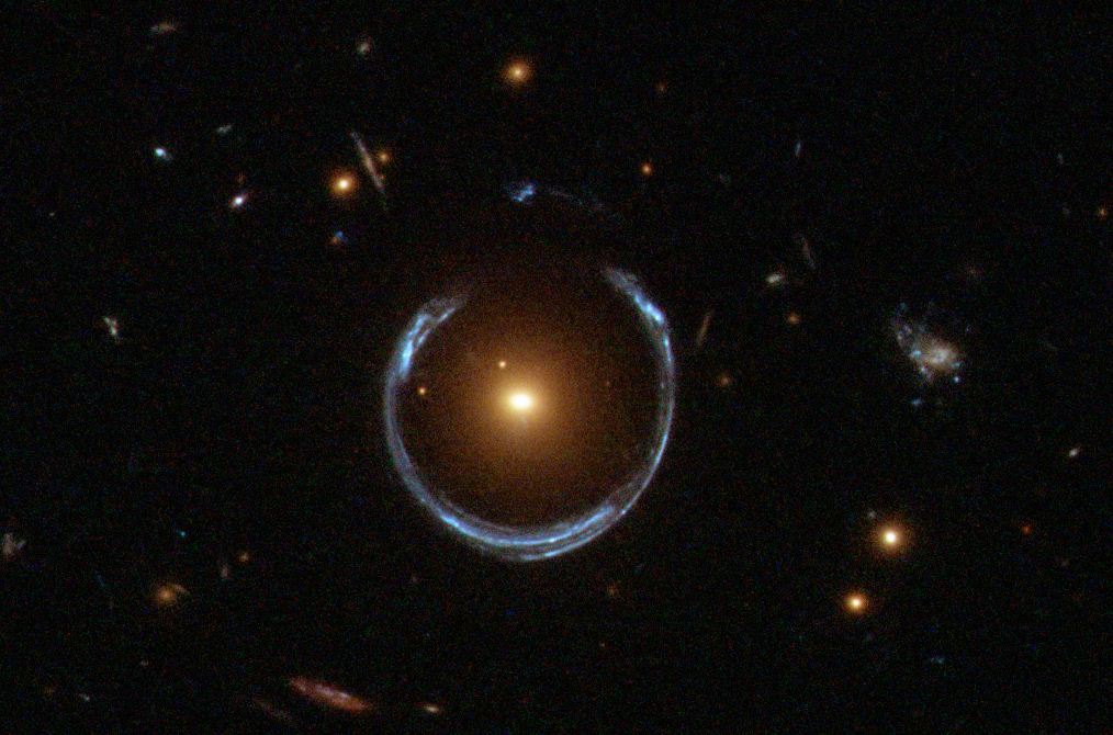 A blue near-complete ring of light encircling a bright orange galaxy — the Cosmic Horseshoe.