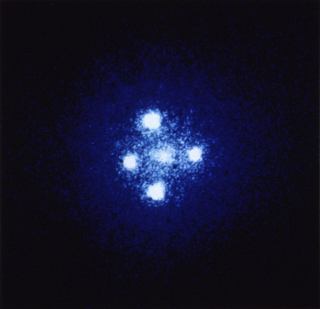 Four bright points of light arranged in a cross around a central galaxy — the Einstein Cross.